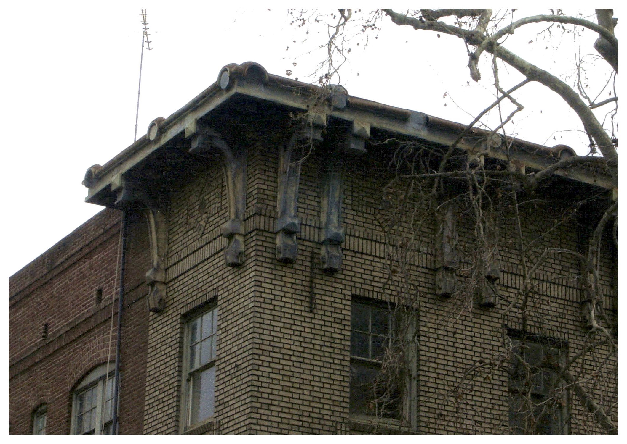 Before: same view of unpainted cornice and uncleaned brick facade at alley corner.